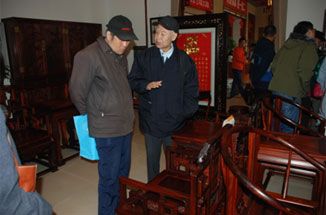 图为红木专家刘鹏教红木爱好者挑选红木家具的窍门