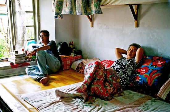 刘小东（左）在拍摄现场，与一位大妈坐在炕上。（剧照）