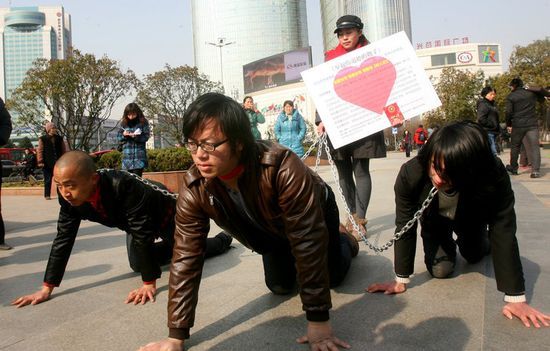 武汉光谷街头，正举行一场名为“举起你道德的皮鞭”的行为艺术，现场有一位女子用铁链牵着在地上爬的三位男士。