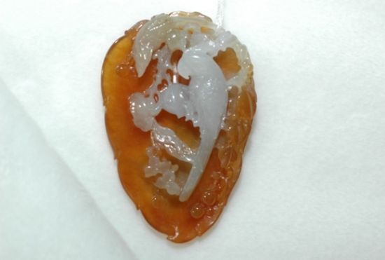 翡翠坠饰。高5.5厘米，宽3.5厘米，厚0.9厘米。种分一般，透明度较好，致密的红皮是其显著特点，上面深浮雕一只鹦鹉，栩栩如生，整个挂坠活气十足，是收藏者最喜欢品玩的一种类型。